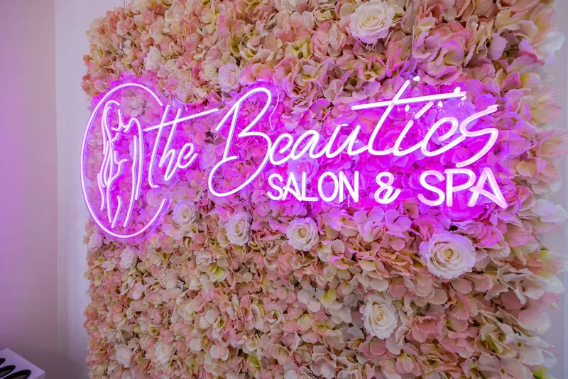 The Beauties Salon & Spa neon sign glowing on the pink flower wall